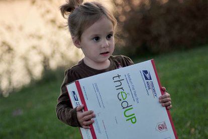 Una niña con uno de los paquetes postales para el intercambio de ropa infantil de la plataforma thredUP.