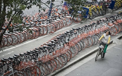 Una señora pasa frente a hileras de bicicletas de pago por uso en Shanghái.