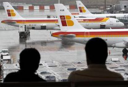 Dos pasajeros observan varios aviones de la compañia Iberia en las pistas del aeropuerto de Barajas. EFE/Archivo