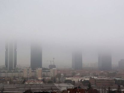 Vista de las Cuatro Torres de Madrid cubiertas por la niebla esta mañana.