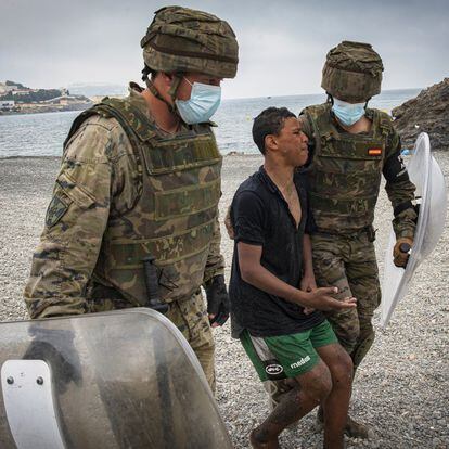 Dos soldados del Ejército de Tierra acompañan a un menor que acaba de salir del agua tras cruzar la frontera nadando. 
