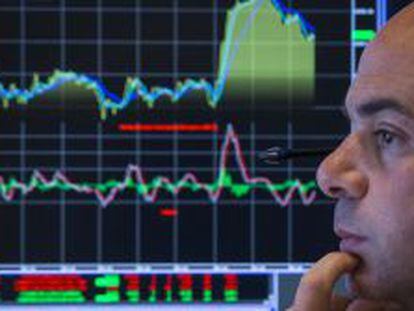 Un trader de la Bolsa de NYSE se hace el intenso con un monitor de fondo. 