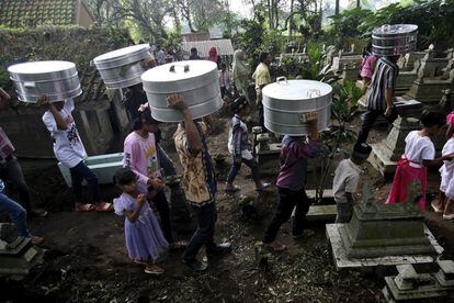 Varias personas cargan con ollas de comida durante una visita al cementerio en la celebración del Nyadran antes de la llegada del Ramadán en Cepogo, Indonesia.