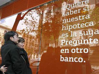 Una pareja observa el anuncio de una hipoteca situado en el exterior de una oficina bancaria.