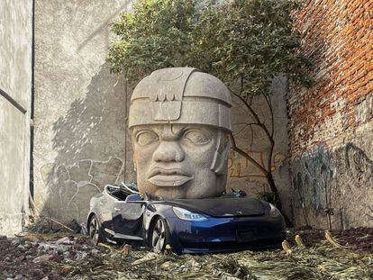 La réplica de una cabeza olmeca aplasta un auto Tesla, en una obra de arte de Chavis Mármol.