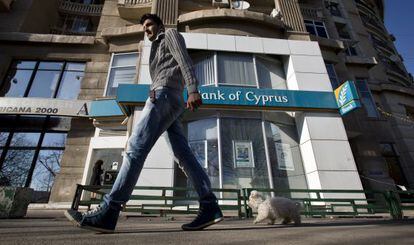 Un hombre pasa con su perro ante una sede del Banco de Chipre.