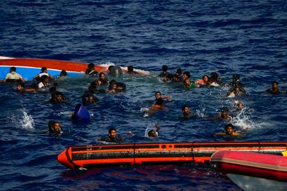 Los migrantes que viajaban a bordo de la patera volcada nadan junto a ella momentos antes de ser rescatados por la tripulación de la ONG española Open Arms.
