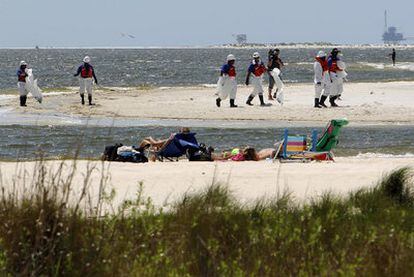 Un grupo de personas toma el sol en una playa del estado de Alabama (EE UU) ante la presencia de un equipo de limpieza del vertido de crudo.