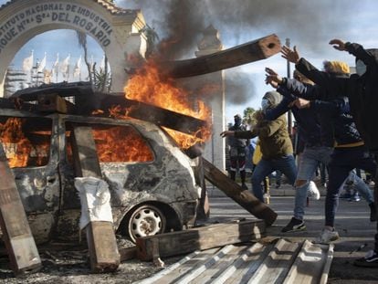 Un grupo de trabajadores lanza vigas de madera a un coche ardiendo.