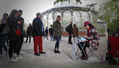Varias personas esperan mientras Nuria Herrera escribe en el Retiro, este sábado.