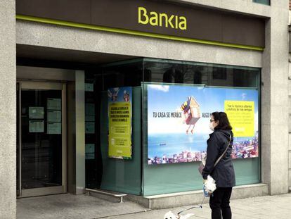 Una mujer pasea con un perro frente a una sucursal de Bankia un día después de que Banco Central Europeo (BCE) haya especificado que decidirá 