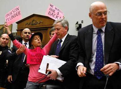 Henry Paulson (derecha) abandona el Congreso de EE UU entre las protestas de una activista.