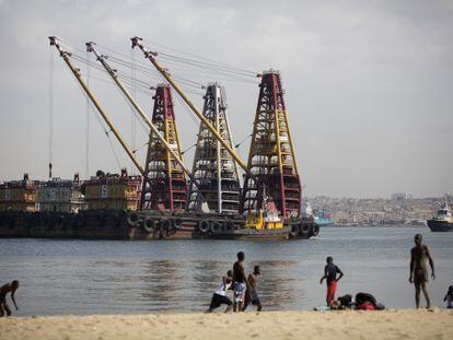 Una barcaza cargada de grúas anclada frente a una playa de Luanda