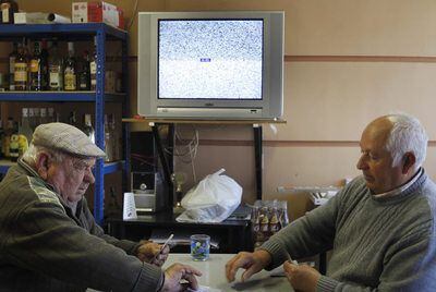 Dos vecinos juegan una partida de cartas ante la televisión sin señal de un bar de Valdaracete.