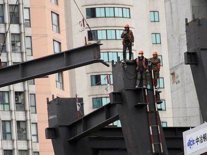 Unos trabajadores contemplan cómo una grúa eleva una estructura en una obra en Shanghái el viernes pasado