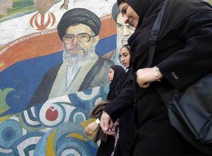 Tres mujeres caminan por delante de un mural de los ayatolás Alí Jamenei (izquierda) y Jomeini en Teherán.