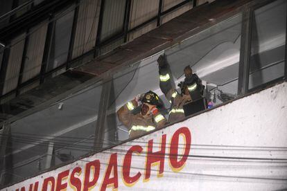 Una pareja de bomberos retira cristales dañados de un edificio en Ciudad de México.