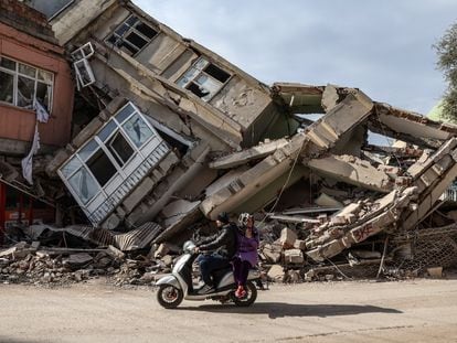 Una pareja en moto pasa por delante de edificios derruidos por los terremotos, este domingo en Adiyaman.