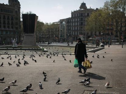 Una persona camina cargado con la compra por plaza Catalunya donde solo quedan las palomas.