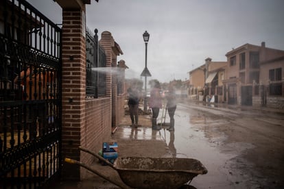 Un vecino limpia con agua el barro de su casa en la calle Madrid.