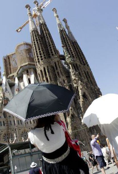 Unas turistas se protegen del intenso calor con paraguas ante la basílica de la Sagrada Familia de Barcelona.