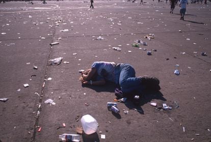 Un asistente al festival de Woodstock 99 duerme bajo el sol en una explanada llena de restos de basura.