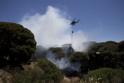 Un helicópterio tira agua a una rebrote del fuego cercano al Parador Nacional de Mazagón.