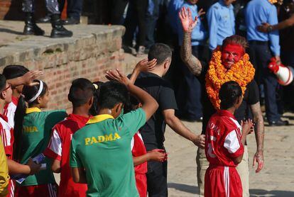 El exfutbolista inglés David Beckham (d) saluda con la cara pintada de rojo tras ser obsequiado con guirnaldas durante su visita a los estudiantes de una escuela que resultó dañada durante el terremoto del pasado 25 de abril, en Bhaktapur (Nepal).