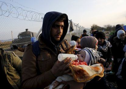 Un refugiado sirio alimenta a su hijo frente a una valla en la frontera cerca de la aldea griega de Idomeni.
