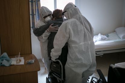 Dos personas ayudan a una mujer mayor a sentarse en una silla de ruedas en una residencia geriátrica de Barcelona, en abril.