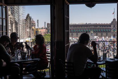 Turistas sentados en la terraza de un restaurante frente a la explanada del Zócalo de la Ciudad de México.