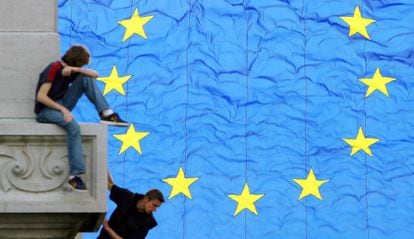 Dos jóvenes, en un edificio junto a una bandera gigante de la UE en Bruselas.