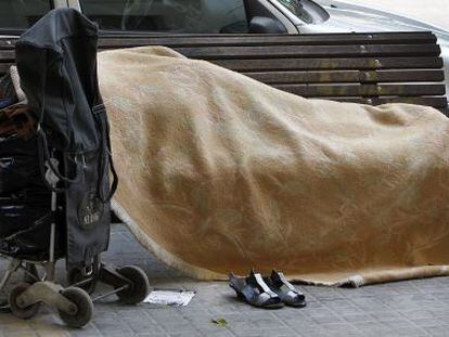 Un indigente duerme sobre un banco p&uacute;blico en Valencia.