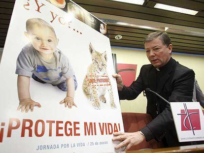 El portavoz de la Conferencia Episcopal, Juan Antonio Martínez Camino, coloca el cartel de la campaña contra el aborto.