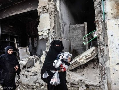 Un par de mujeres caminan con sus hijos frente a un edificio en ruinas de la ciudad siria de Raqa.  
