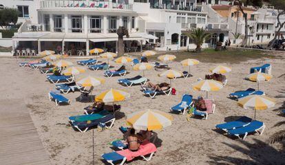 Varias personas toman el sol en la Cala Santandría de Menorca. 