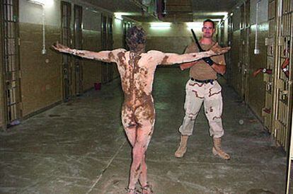 Un preso iraquí, desnudo y cubierto por una sustancia ocre, ante un soldado de EE UU con una porra en Abu Ghraib.