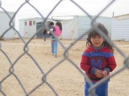 Una ni&ntilde;a mira a c&aacute;mara al otro lado de la verja del campo de refugiados de Zaatari, en Jordania.