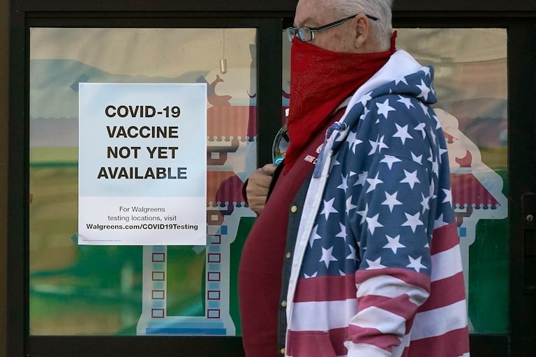 Un peatón con un pañuelo pasa delante de un cartel que indica que la vacuna de la covid-19 no se vende en las farmacias Walgreens.