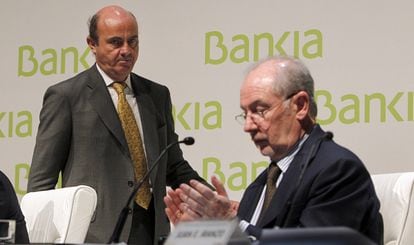 Luis de Guindos (a la izquierda), pasa por detrás de Rodrigo Rato, que aplaude su intervención en el Encuentro Financiero Internacional de Bankia de 2012.