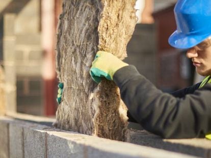 Un trabajador de la construcción coloca una manta de aislamiento térmico en la cavidad de un muro.