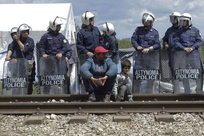 Un hombre y su hijo esperan junto a la policía en el campo de refugiados de Idomeni (Grecia).