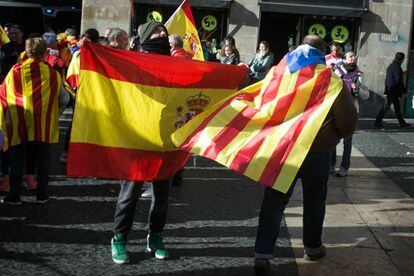 Un ciudadano con una bandera estelada colgada del cuello cruza la plaza Sant Jaume junto a otras personas que portan banderas españolas, en Barcelona.