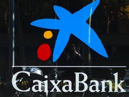Dos personas pasan por delante de una oficina de CaixaBank, en Barcelona.
