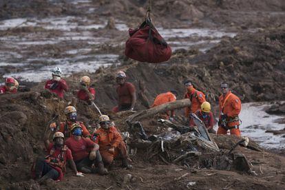 Un grupo bomberos brasileños observan el cuerpo de una persona al que rescataron del lodo.