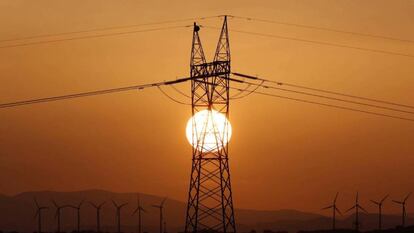 Torre del tendido eléctrico, en primer término, y molinos de viento al fondo.