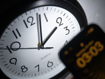 Un reloj analógico junto a un teléfono móvil que marca la hora.