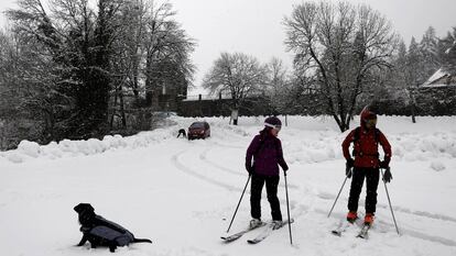 Dos esquiadores junto a un perro disfrutan entre la nieve del aparcamiento parking de Roncesvalles completamente cubierto.