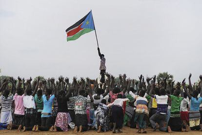 Un hombre ondea la bandera de Sudán del Sur mientras niños ensayan un baile para el día de la independencia.