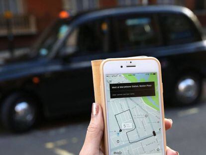 Una mujer usa la aplicación de Uber frente a un taxi londinense. 